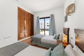 A bedroom with two beds, a wooden wardrobe, a large window with curtains, and a view of the outside. - Villa Dafne by Escape Home (Playa Blanca)