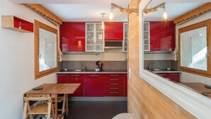 Een kleine keuken met rode kastjes, een houten tafel en een ingebouwde oven.