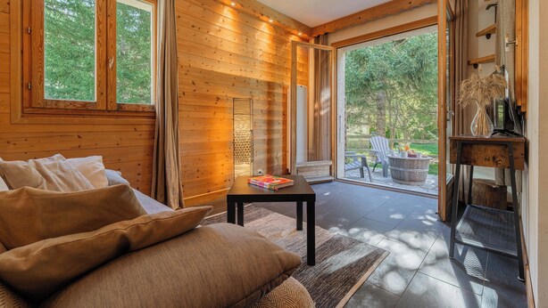 Een houten interieur met een bank, een tafel met een boek en uitzicht op de omgeving.