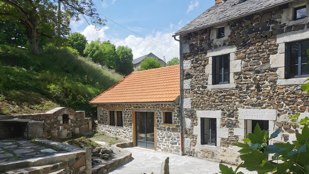 A stone building with a tiled roof, a stone staircase, and a garden area.