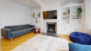 A living room with a sofa, a coffee table, a fireplace, a TV, and built-in shelving. - Bright 2BR Apt- 11 min walk to Kensington Palace (London)