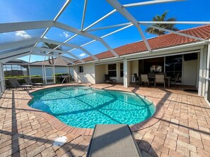 A swimming pool with a glass enclosure, lounge chairs, and a patio area. - Villa Seas The Day - pool, cozy, office (Cape Coral)