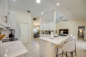 Una cocina moderna con armarios blancos, una isla central con taburetes y un comedor visible al fondo.