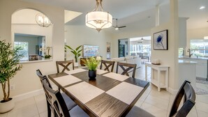 A spacious dining area with a large table, chairs, and a chandelier. There is a view of the living area in the background. - Villa Seas The Day - pool, cozy, office (Cape Coral)