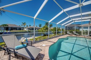 A covered outdoor swimming pool area with lounge chairs and a view of a residential neighborhood. - Villa Seas The Day - pool, cozy, office (Cape Coral)