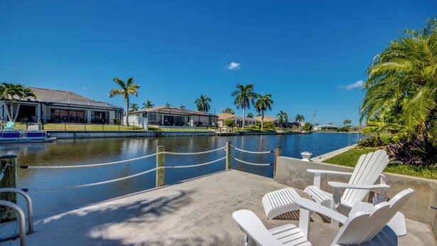 A waterfront property with a pool, lounge chairs, and a boat dock. - Villa Seas The Day - pool, cozy, office (Cape Coral)