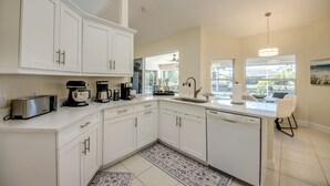 A modern kitchen with white cabinetry, a built-in dishwasher, and a large island with a sink. - Villa Seas The Day - pool, cozy, office (Cape Coral)