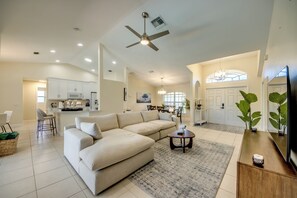 A spacious living area with a large beige sectional sofa, a dining area with a chandelier, and a kitchen in the background. - Villa Seas The Day - pool, cozy, office (Cape Coral)
