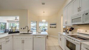 A modern kitchen with white cabinetry, a central island, a dishwasher, a stove, and a microwave. - Villa Seas The Day - pool, cozy, office (Cape Coral)
