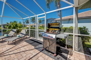 A covered outdoor area with a barbecue grill, lounge chairs, and a view of a residential neighborhood. - Villa Seas The Day - pool, cozy, office (Cape Coral)