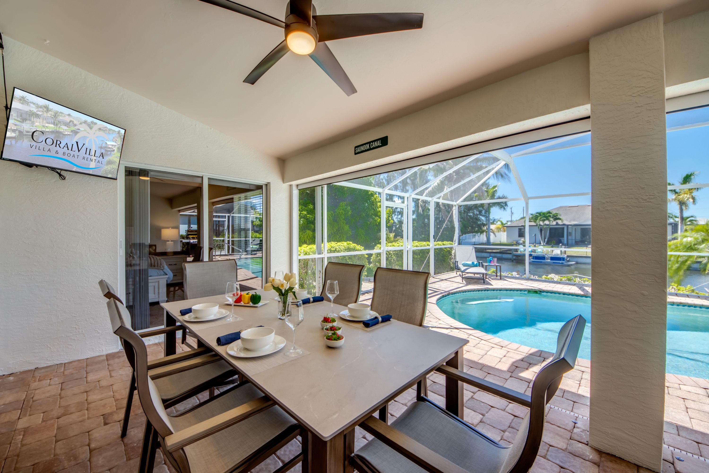 A dining area with a table set for two, a ceiling fan, and a view of a swimming pool.