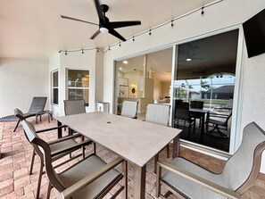 A covered patio with a table and chairs, a ceiling fan, and a view through large glass doors. - Villa Seas The Day - pool, cozy, office (Cape Coral)