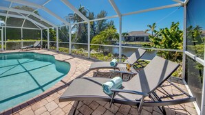 A covered outdoor swimming pool with lounge chairs and a view of a lake and surrounding greenery. - Villa Seas The Day - pool, cozy, office (Cape Coral)