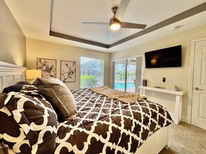 Une chambre à coucher comprenant un lit, un ventilateur de plafond, des œuvres d’art et un téléviseur.
