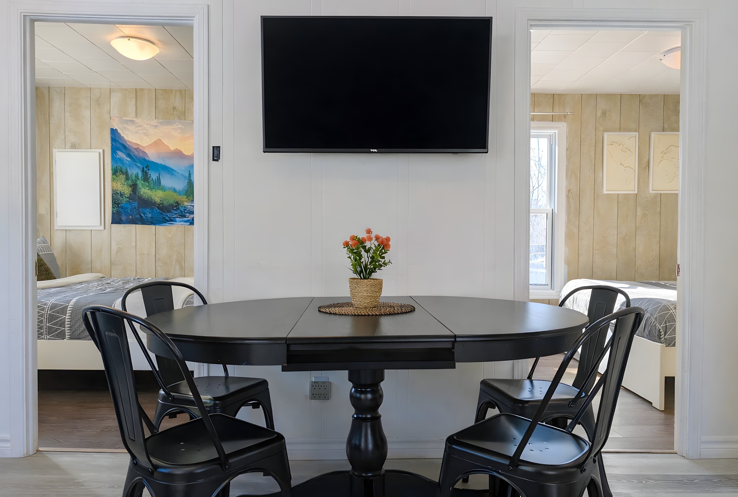 A dining area with a round table, four chairs, a flat-screen TV mounted on the wall, and a painting on the wall.