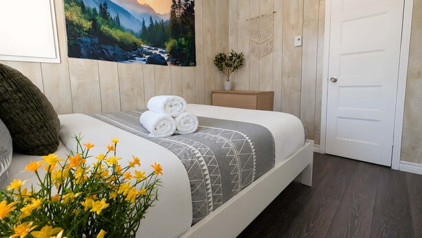 Um quarto com cama, um quadro, uma planta e uma porta.