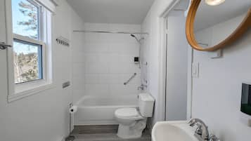 A modern bathroom with a bathtub, toilet, and sink, featuring white tiles and a large window.