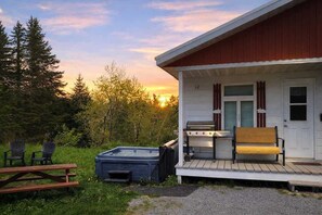 A cabin with a deck, a hot tub, and a picnic table.
