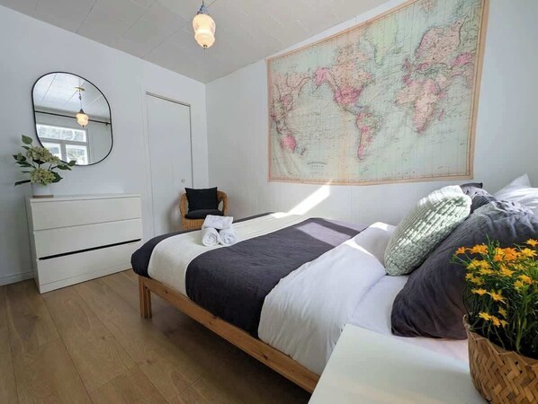 Une chambre à coucher avec un lit, une commode, une chaise, une carte accrochée au mur et une plante.