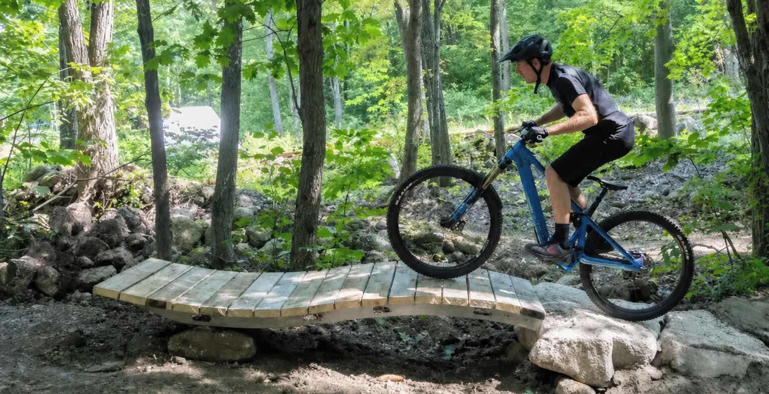 A person riding a mountain bike on a wooden bridge in a forested area.