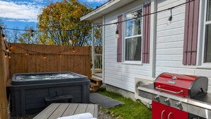 Un patio trasero con un jacuzzi, una parrilla y una terraza de madera.