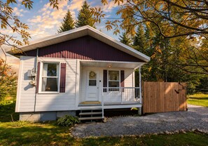 A single-story house with a front porch, a wooden fence, and a gravel driveway. - Le Tremble · 4 pers · Spa · Massif & MSA · 10D (La Côte-de-Beaupré)