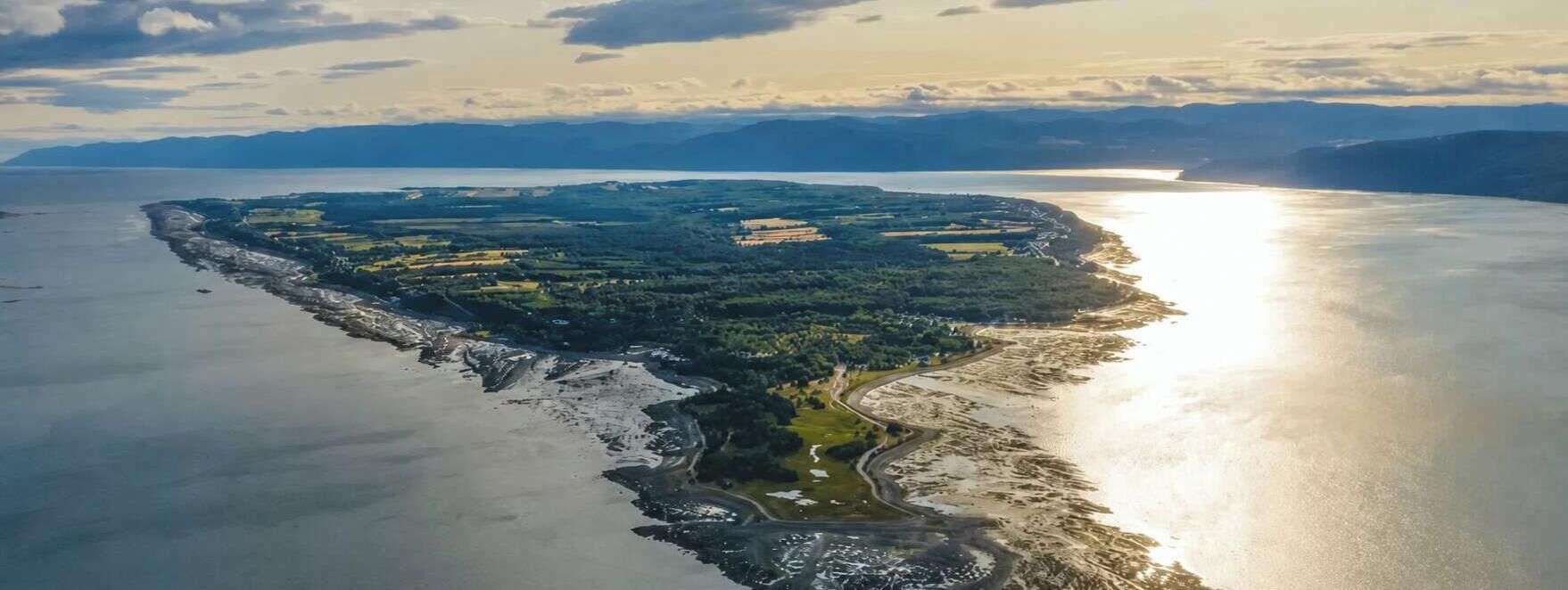 An aerial view of a coastal area with a mix of natural and developed land, including a body of water and a winding road.