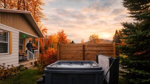 Ett bubbelbad i en trädgård med ett trähäck, ett hus och höstlöv.