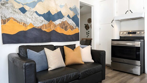 Ett modernt vardagsrum med en svart lädersoffa, en stor abstrakt målning och en köksdel med en inbyggd ugn.