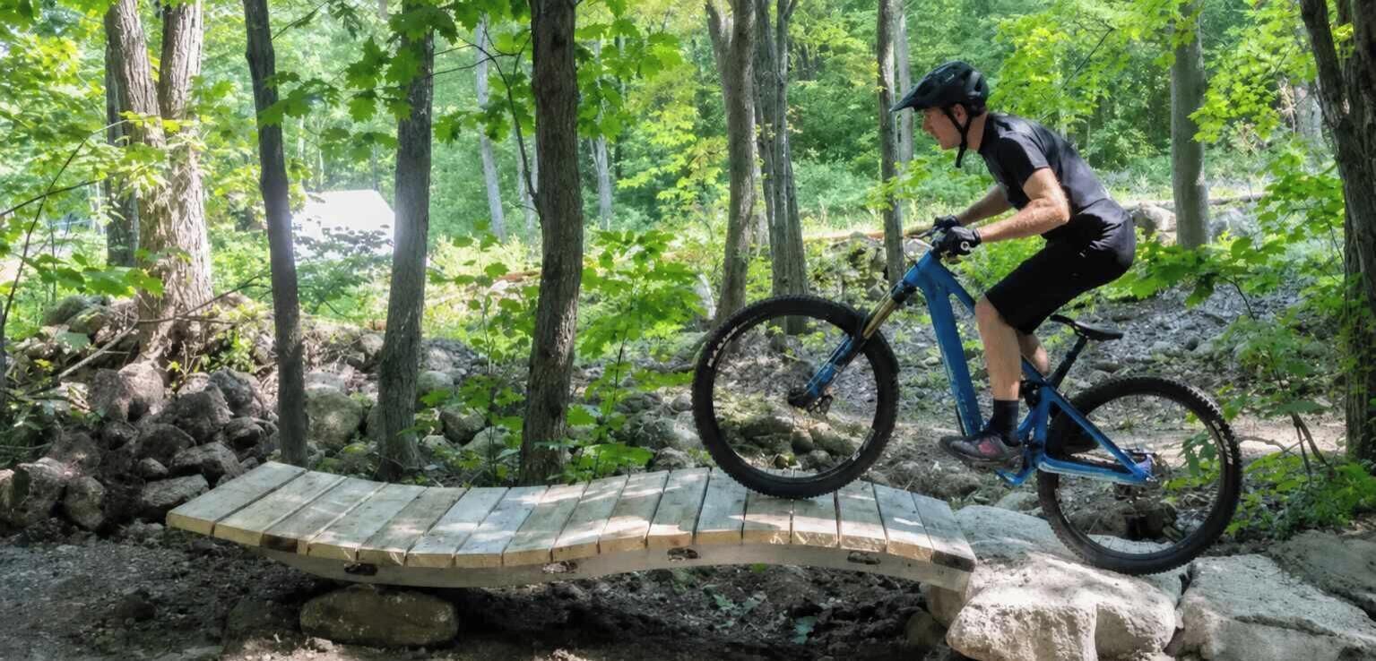 A person riding a mountain bike on a wooden bridge in a forested area.