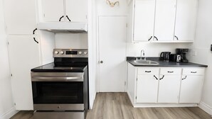 Une cuisine moderne avec des meubles blancs, un four en acier inoxydable, un évier et une machine à café.