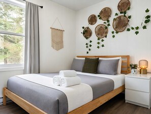 Una cama bien hecha con edredón gris y blanco, un cabecero de madera y una mesita de noche con una lámpara.