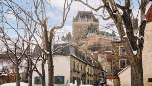 A historic building with a prominent tower and multiple windows, surrounded by snow-covered trees and other buildings. - Le Grand Pin · 6 pers · Spa · Massif & MSA · 16 (Saint-Tite-des-Caps)