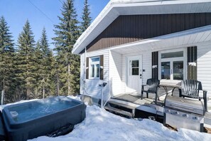 A cabin with a hot tub, outdoor seating, and a view of a forest. - Chic Shack with spa - near Massif Charlevoix & MSA (Saint-Tite-des-Caps)