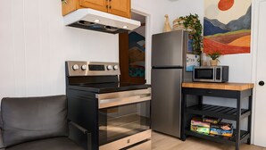 A compact kitchen with a stove, oven, refrigerator, microwave, and a small wooden table. - Le Grand Pin · 6 pers · Spa · Massif & MSA · 16 (Saint-Tite-des-Caps)