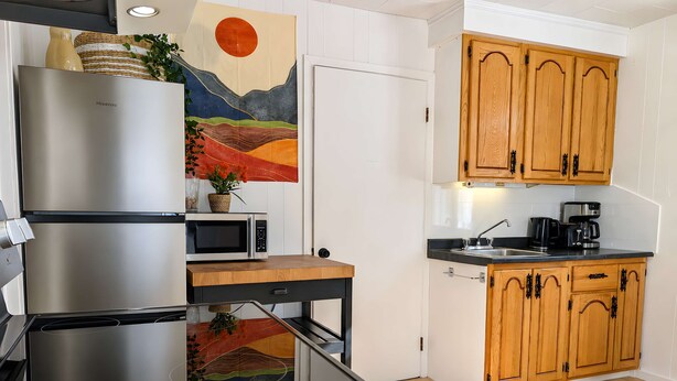 A modern kitchen with stainless steel appliances, wooden cabinets, and a decorative wall piece. - Le Grand Pin · 6 pers · Spa · Massif & MSA · 16 (Saint-Tite-des-Caps)