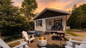 A cozy outdoor seating area with Adirondack chairs, a fire pit, and a hot tub. - Le Grand Pin · 6 pers · Spa · Massif & MSA · 16 (Saint-Tite-des-Caps)