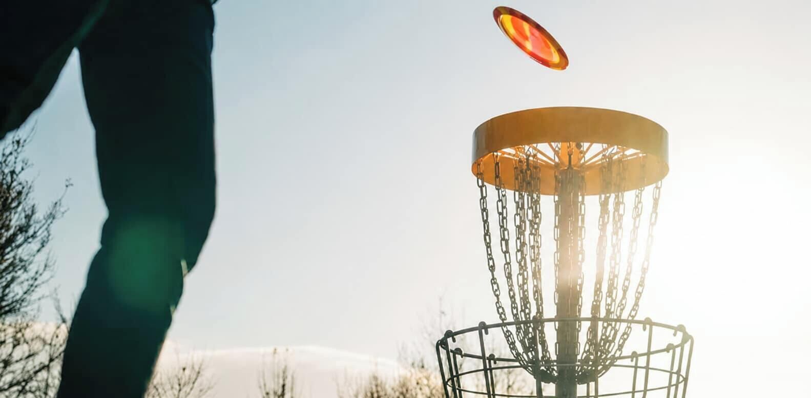 A disc golf basket with chains and a disc in mid-air.