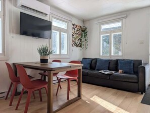 A modern living room with a black leather sofa, red chairs, a wooden dining table, and a flat-screen TV mounted on the wall. - Chic Shack with spa - near Massif Charlevoix & MSA (Saint-Tite-des-Caps)
