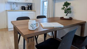 Moderni keittiö, jossa on valkoiset kaapit, puinen ruokapöytä, kahvimuki ja avoinna oleva kirja.