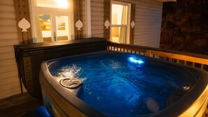A hot tub with a built-in heater, positioned outdoors next to a house with a wooden deck.