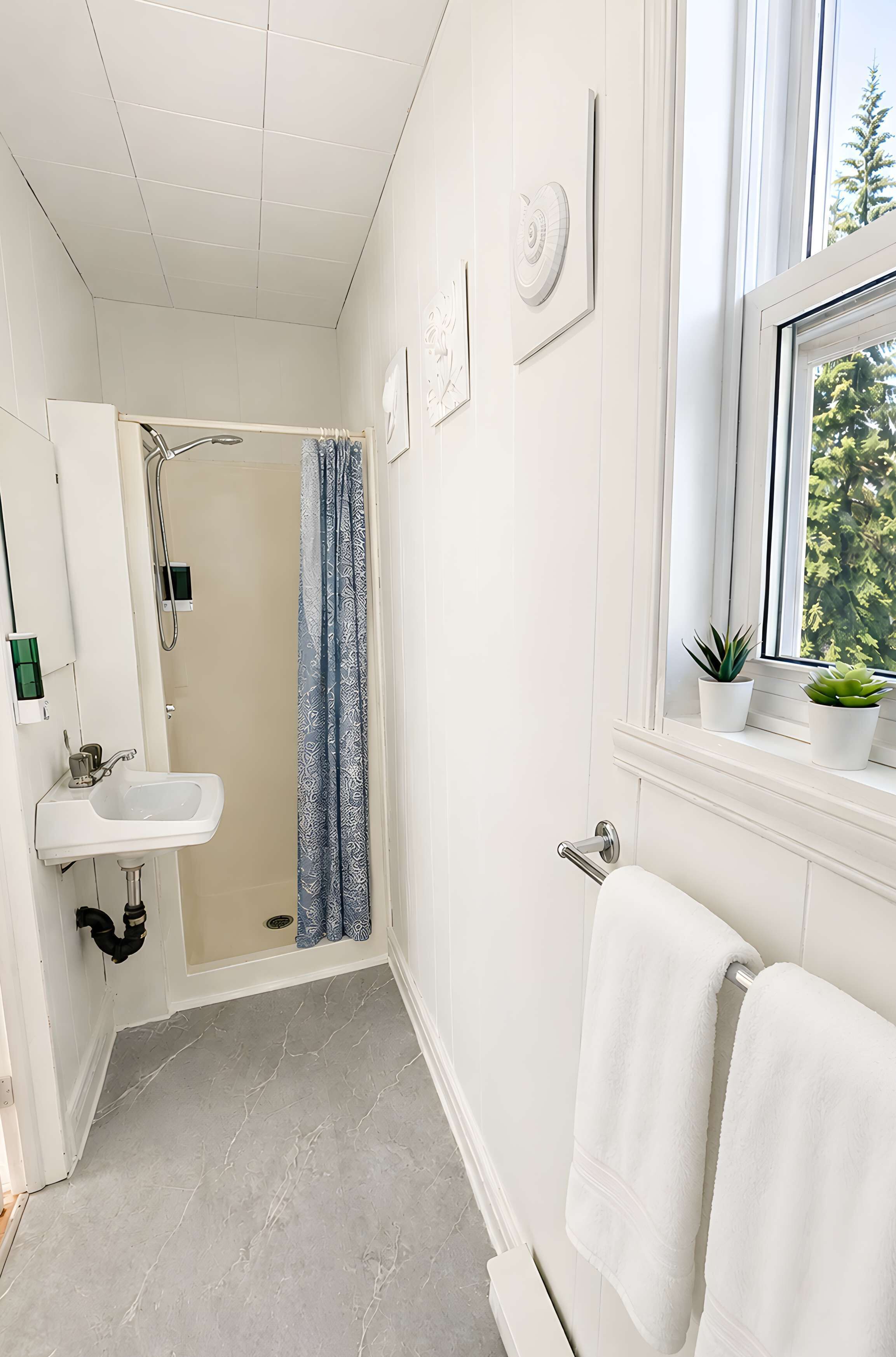 A bathroom with a shower, sink, towel rack, and a window with plants.