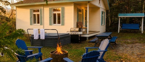 Una cabaña pequeña con jacuzzi, mobiliario exterior y una chimenea.