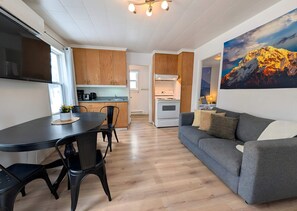 Ett modernt kök med träskåp, en matplats med bord och stolar, en grå soffa med kuddar och en stor målning av ett berg.