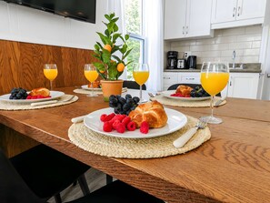 Desayuno con cruasanes, fruta y zumo de naranja sobre una mesa de madera en una cocina moderna.
