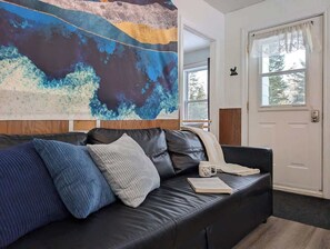 Een moderne woonkamer met een zwarte leren bank, een groot abstract schilderij en een deur met een witte gordijn.