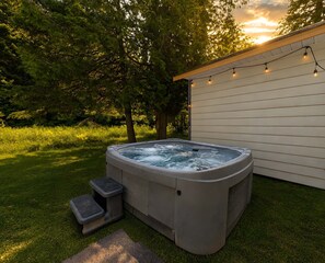 Een jacuzzi in een achtertuin met een houten terras en lichtjes.