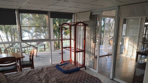 Een slaapkamer met een bed, bureau en stoel, grote ramen en een schuifdeur die leidt naar een buitenruimte.