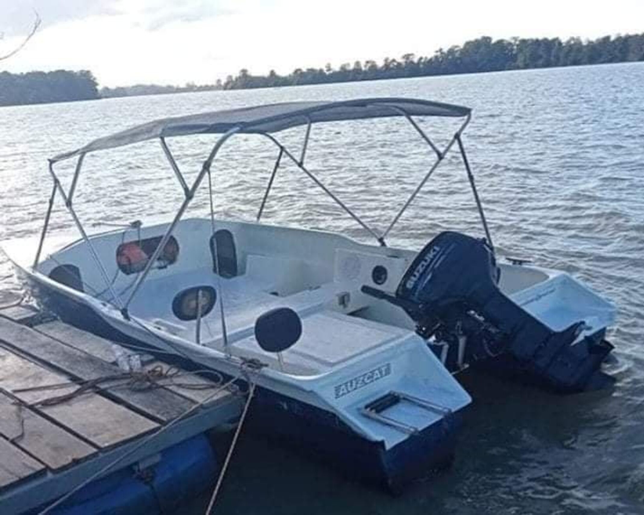 Un pequeño barco motor con toldo, un motor Suzuki y casco azul, atracado en un muelle de madera.