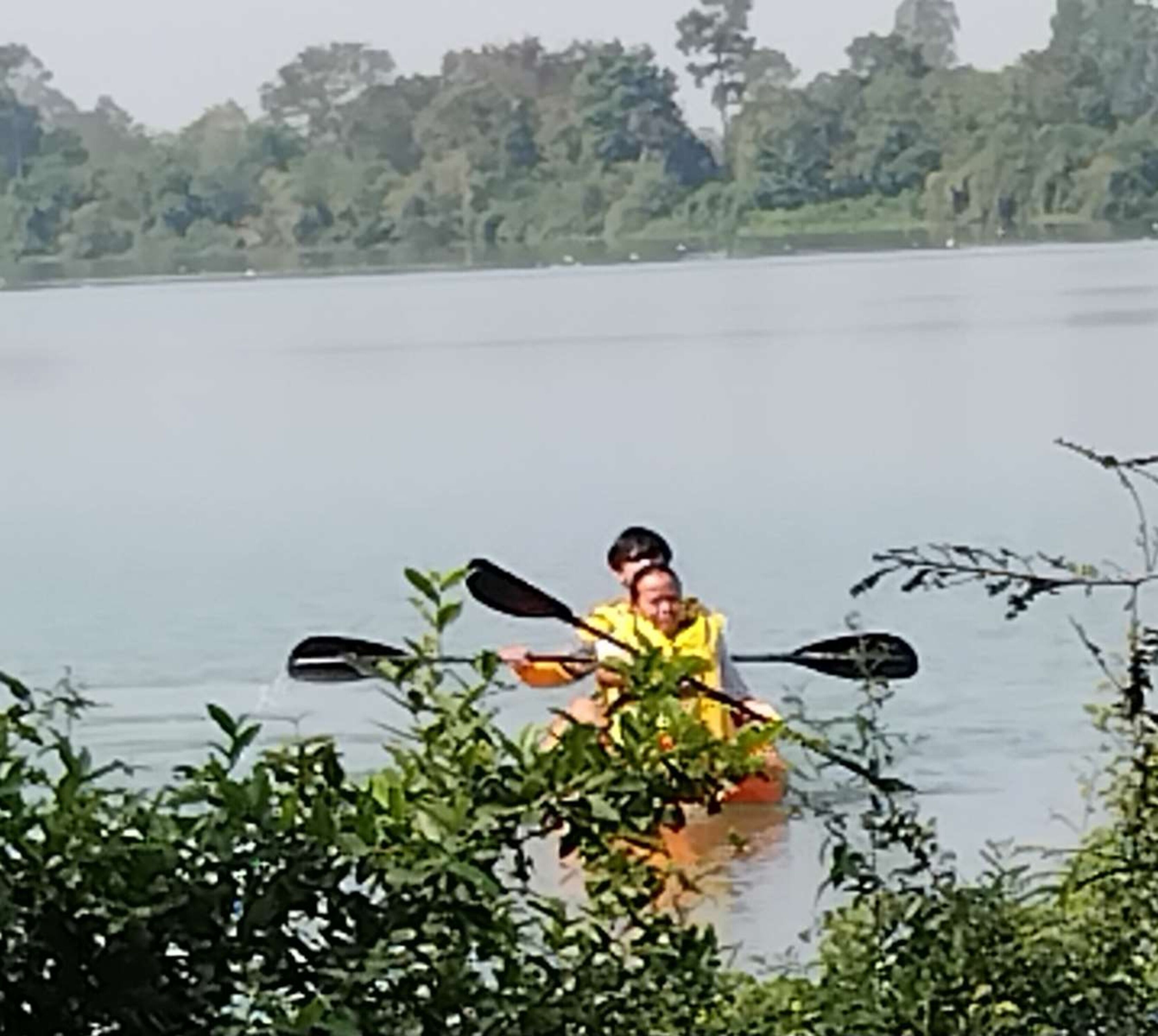 Une personne pratiquant le kayak sur un lac, entourée de verdure.